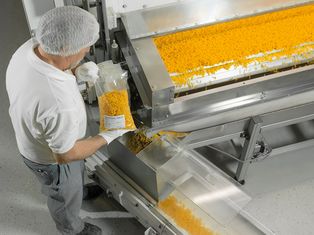 Mitarbeiter in weißer Arbeitskleidung und Haarnetz steht vor einer Nudelproduktionsanlage