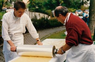 Two men roll out pasta dough on a long table with large rollers as part of a world record attempt