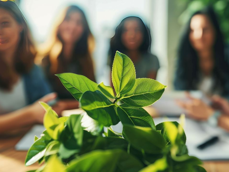 Group of five people in the background, fresh green leaves on a table in the foreground