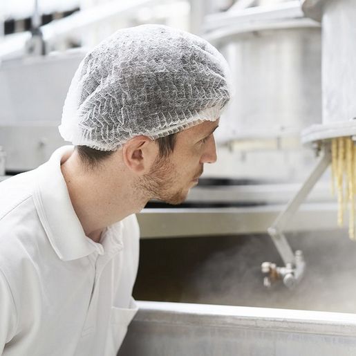 Produktionsmitarbeiter mit Haarnetz schaut auf eine Nudelmaschine in einer Produktionsanlage