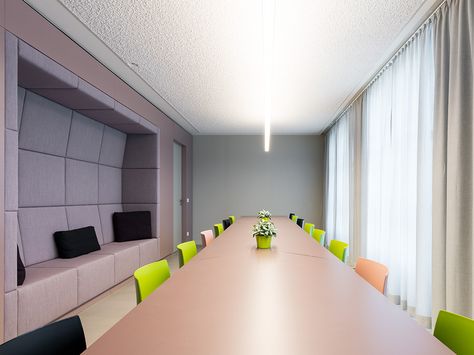 Moderner Besprechungsraum mit langem Holztisch, bunten Stühlen und eingebauten Sitznischen an der Wand