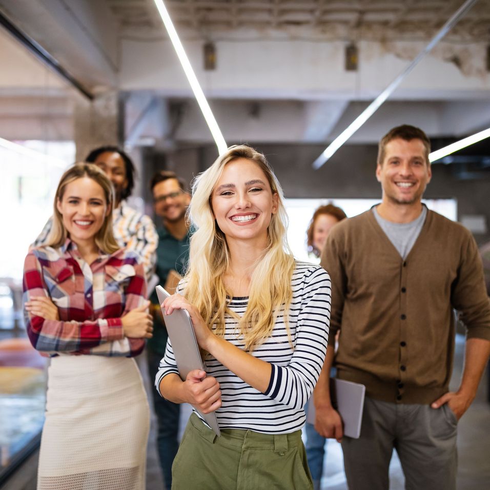 Fünf lächelnde Erwachsene in einem modernen Büro, die in die Kamera schauen