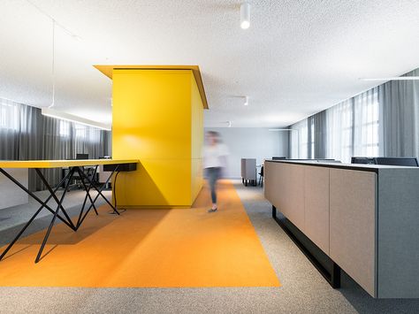 Moderner offener Besprechungsraum mit gelber Wand, orangefarbenem Teppich und großen Fenstern