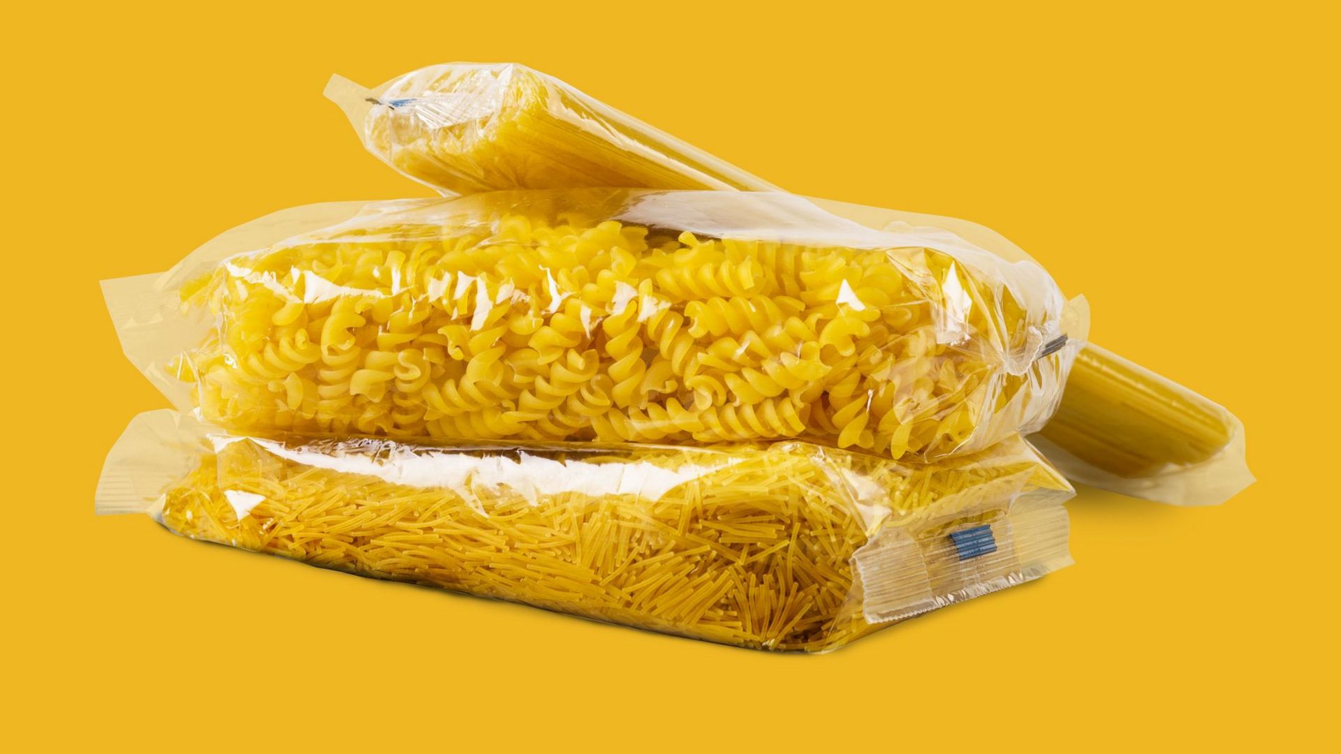 Several bags of pasta in transparent packaging on a yellow background.