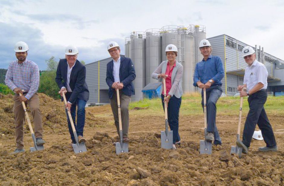Six people with hard hats and spades at the ground-breaking ceremony for the new warehouse with logistics center, in the background buildings