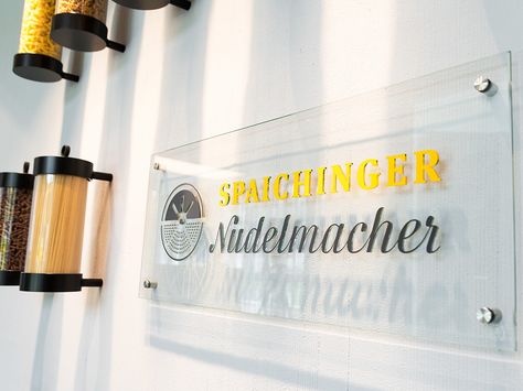 Logo 'Spaichinger Nudelmacher' auf transparentem Schild an Wand, daneben Gefäße mit verschiedenen Nudelsorten